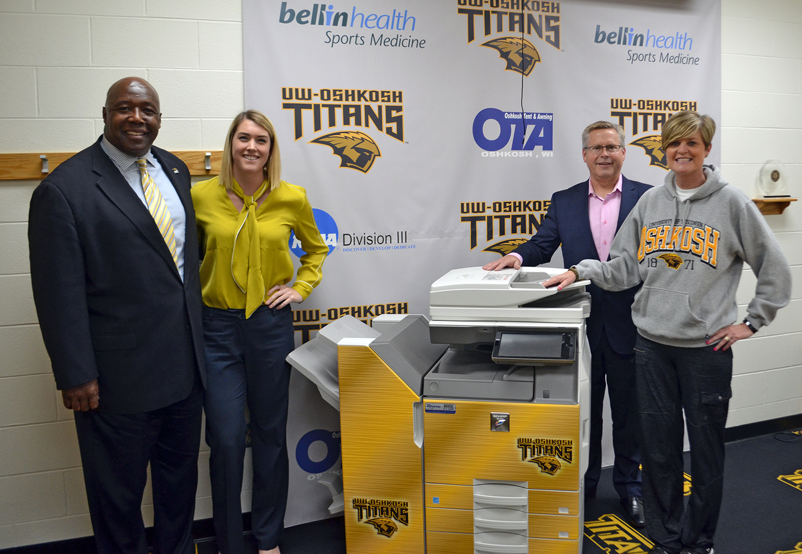 Rhyme Director of Marketing and President pose with UW-Oshkosh Director of Athletics next to the new MFP sold by Rhyme
