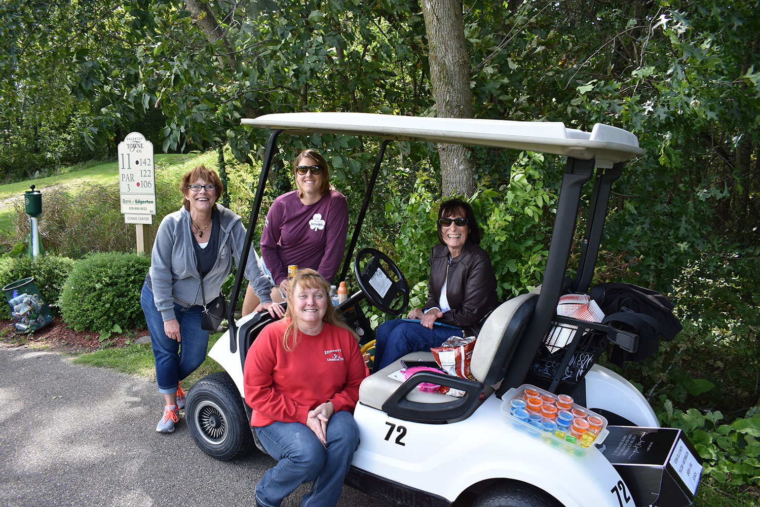 Four volunteers sitting in and around a golf cart at the Steve Ennis Memorial Golf event