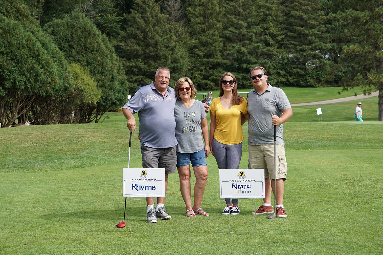Four golfers stand next to Rhyme Time Scholarship signs at the Steve Ennis Memorial Golf Event