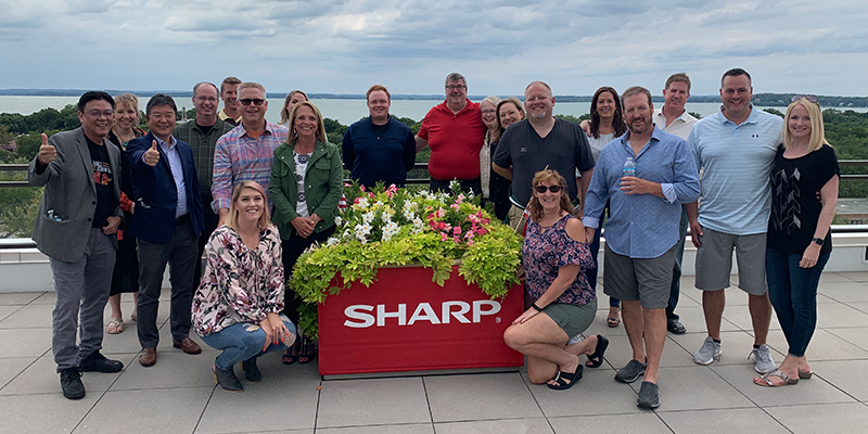 Rhyme team members pose around a planter with the Sharp logo on it after being recognized as elite dealers