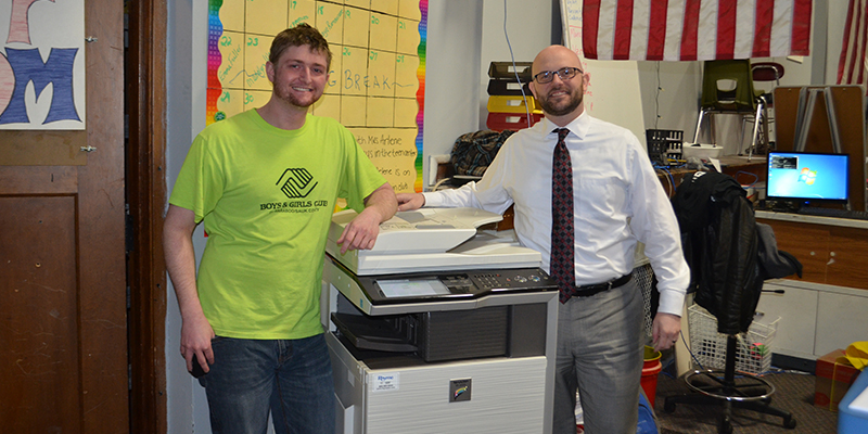 A Rhyme employee and Boys & Girls Club volunteer stand next to a copy machine donated by Rhyme
