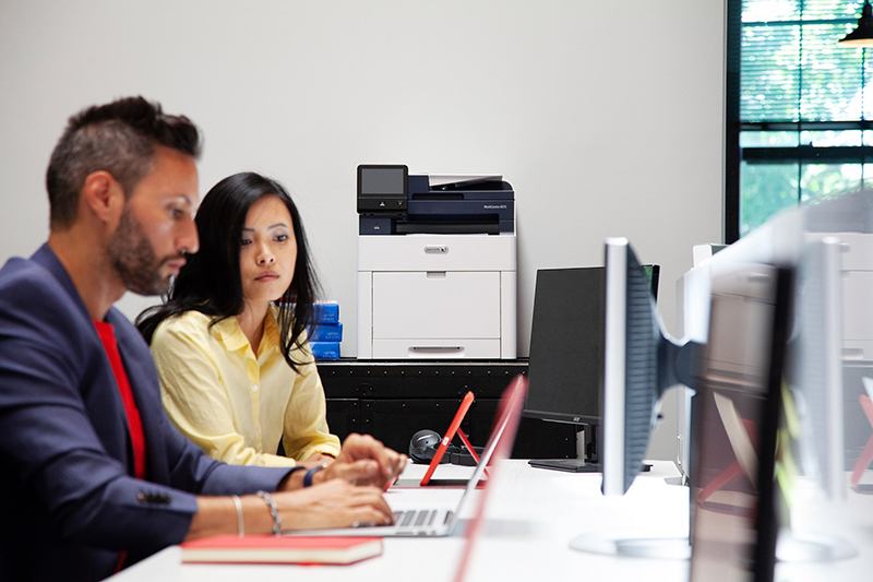 Employees working and talking in an office with a Xerox multifunction device